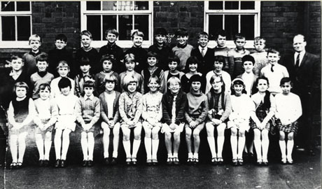 Photograph of a group fifteen boys and twenty two girls of Easington Colliery Junior School, posed in the school yard with their male teacher; the children are aged approximately ten years; behind the children written on the wall of the school is ......ber 1968