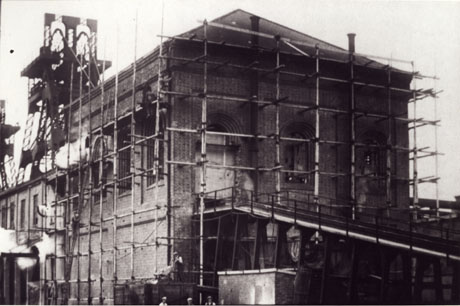 Photograph of one of the colliery buildings close-up with scaffolding round it; the winding gear can be seen on the building