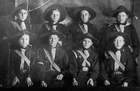 Photograph showing eight girls posed in two rows; they are wearing a uniform of dark blouse, sash across the chest and a hat with a brim; they have beeb identified as First Girl Guides in Easington Colliery