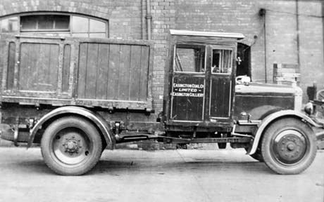 Photograph of a motor lorry with the words Easington Coal Co. Limited Easington Colliery on its side, parked in front of a large brick building; it has a wooden container on its back; it has been described as a Coal Waggon