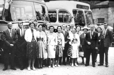 Photograph of twelve women, six men and one small girl, aged approximately nine years, standing in a group in front of the bonnets of two single-decker motor buses; one of them has the sign Excursion on it; they have been identified as taking part in an outing from Easington Colliery