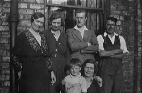 Photograph of two women and two men standing in front of the window of a house; in front of them, the head and shoulders of a woman and a child can be seen; they have been identified as being in Office Street, Easington Colliery