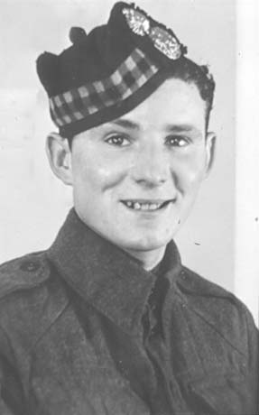 Photograph of the head and shoulders of a young man wearing battle dress and a military cap with tartan and two badges on it; he has been identified as Dennis Donninni, V.C., of Easington Colliery