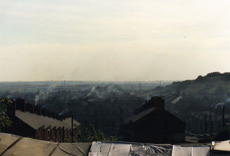 Photograph taken from above of terraced houses running down a hillside away from the camera; smoke can be seen coming from the houses, the details of which are difficult to discern as the photograph is rather dark; a hillside in the right and the horizon in the distance can be seen; the view has been identified as that of Easington Colliery