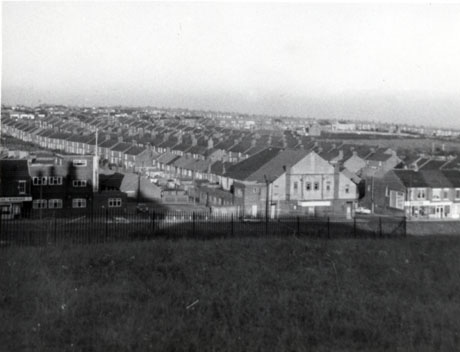 Photograph, taken from the slope of a hill, looking out over the roofs of rows of houses running away from the camera to the sea; a large chapel-like building and a large college-like building can be seen at the forefront of the houses; the place has been identified as Easington Colliery