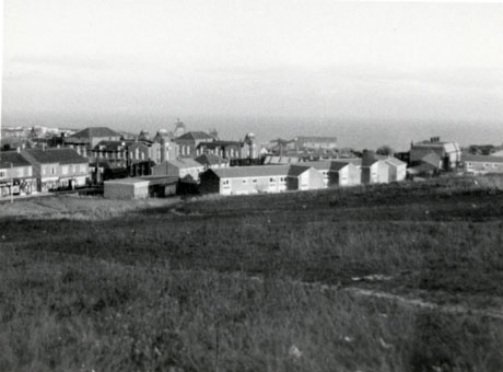 Photograph, taken from a hill, of Easington Junior School and houses surrounding it; beyond the school and the other buildings the sea can be seen; the place has been identified as Easington Colliery