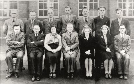 Photograph of eleven men and three women posed in two rows outside a building which may be a school; all the men are dressed in suits and ties and the women are dressed in suits and blouse and skirt; they are middle-aged and may be the teaching staff of a school; they have been identified as being in Easington Colliery
