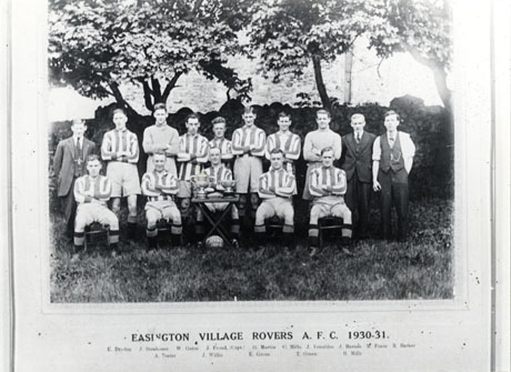 Photograph of the fifteen members of Easington Village Rovers Athletic Football Club 1930- 1931,identified as, back row from left to right: E. Dryden; J. Stenhouse; W. Gates; J. Froud (Captain); G. Martin; C. Mills; J. Venables; J. Barnes; M. Frain; R. Barker; front row from left to right: A. Foster; J. Willis; E. Green; T. Green; R. Mills; the members are posed in front of trees and have two trophies on a table in front of them