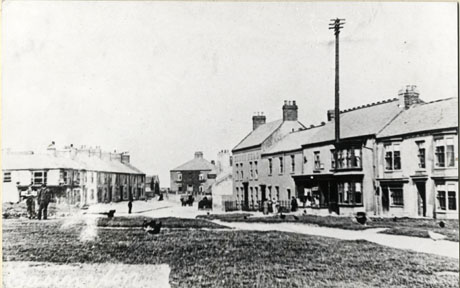 Photograph showing,on the right, a row of shops ending in a public house; beyond this row in the distance a large house can be seen; on the left of the photograph in the distance is a row of terraced houses; in the foreground is an open space; small indistinct figures can be seen dotted around the photograph; the photograph is described as Village Green- View of Cadwell Farm House; it is to be presumed that the farm house is the building in the distance