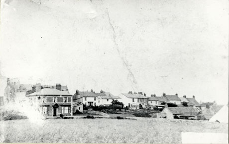 Photograph showing a large house, and the back of a street of houses, in the distance, across a grassed area; the gardens of the street of houses can be seen running down a slope towards another house the roof only of which can be seen; the photograph is identified as Clappersgate, Easington Village