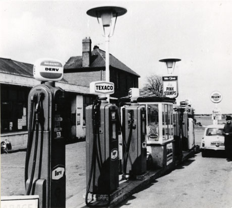 Photograph showing the forecourt of a garage with, in the foreground, five petrol pumps selling Regent Derv, and Texaco Super; a sign offering Pink Stamps can be seen; a car with the registration NBR 902 H is standing in the distance on the forecourt with a man beside it; the garage has been identified as Cockburn's Garage