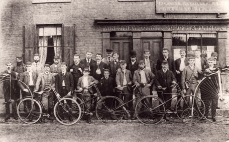 Photograph of twenty five members of Easington Village Cycle Club outside an inn; behind the men can be seen an ordinary window and a large shop window, above which the following words can be read; Wines Hay Corn Good Stabling; above the window, part of a board can be seen with the words: Licensed Retailer Ales Porter Spirits;the men have three bicycles and two penny farthing bicycles in front of them