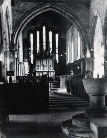 Photograph of the interior of St. Mary's Church, Easington, looking towards the altar, showing the font at the front of the picture, the pews, and the reredos behind the altar