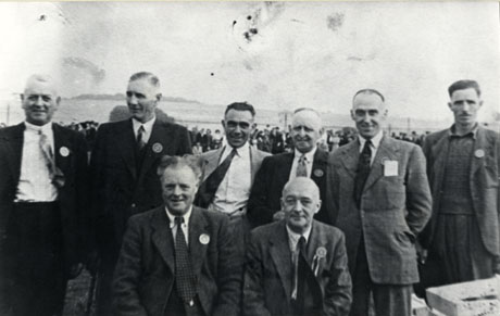 Photograph of seven men described as Organisers Easington County Show; the men all of whom are middle-aged and wearing suits and badges, are photographed with crowds of people in the distance