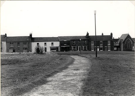 Photograph showing a path through grass leading to a row of five houses with a chapel at the right end of it; the photograph has been identified as Easington Village