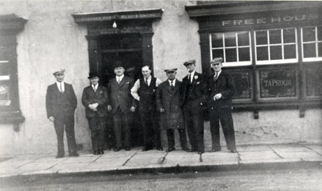 Photograph showing seven men standing outside the entrance to a public house in Haswell; six of the men are formally dressed in suits and ties, the seventh is in shirt sleeves and may be the publican; the facade of the building can be seen and the words Free House and Tap Room can be seen on the window; the words Licensed For Music and Singing can be seen above the door