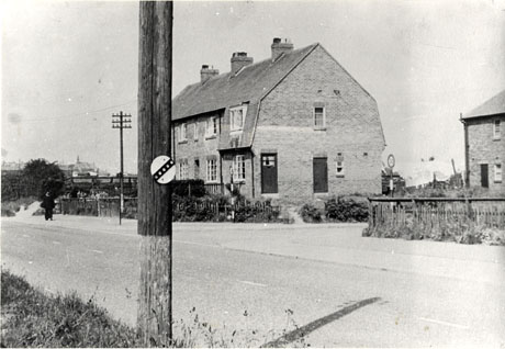 Photograph showing the side and front of the exterior of a house built in the middle years of the twentieth century; the house is photographed from across the road in front of the house; the photograph has been identified as Council Offices, Haswell Plough; a small indistinct figure can be seen walking away from the camera to the left of the picture; in the distance the roof of an ecclesiastical building can be seen