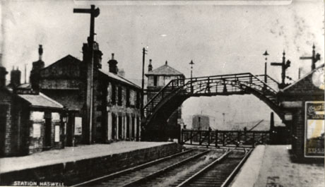 Postcard photograph entitled Station, Haswell, showing the station buildings on one platform of the station, the track, the bridge over the line, the signal box, the level crossing gate, and part of the other platform
