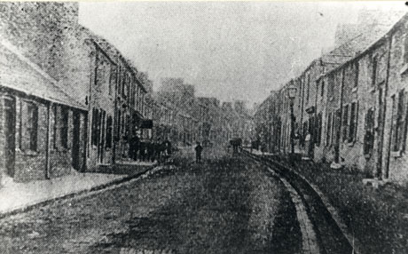 Photograph, entitled Haswell, showing a street lined on either side with terraced houses receding into the distance; a number of indistinct figures can be seen standing on the pavement and in the road; the photograph is, as a whole, very indistinct and may have been originally printed in a newspaper; the date of the photograph has been identified as 1890
