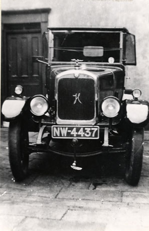 Photograph of the radiator, bonnet and windscreen of a motor car standing in front of a wall and door; the radiator of the car has an H on it and the registration number of the car is NW-4437; the car has been described as The Second Car in Haswell, A Hillman, 1925