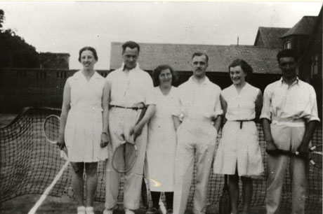 Photograph of three men and three women in tennis whites standing in front of a tennis net with roofs of buildings behind them;three of the people are holding tennis racquets;the photograph is described is described as Haswell Tennis Club,1935