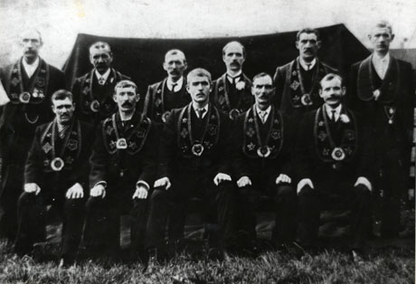 Photograph of eleven men wearing collars round their necks and posed with a tent behind them; the photograph is described as Haswell Independent Order of The Good Templars, 1909