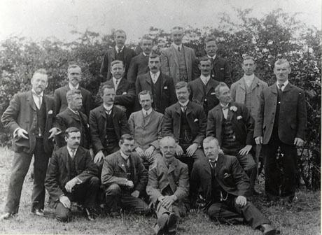 Photograph of twenty men posed in four rows in front of trees; all are wearing suits and ties and are described as The First Co-Op Committee in Haswell