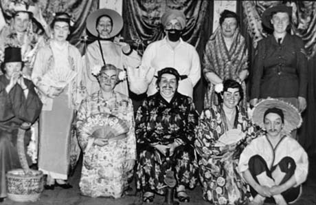 Photograph of eleven women posed in front of draperies; they are dressed as Chinese, Indians and as a member of The Royal Canadian Mounted Police; one is dressed a snake charmer; they have been described as Haswell Women's Institute Entertainers