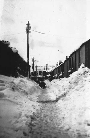 Photograph of two rows of terraced houses with piles of snow in front of each and a path dug out of the snow in the middle; snow-covered fields can be seen in the distance; the houses have been identified as Station Street, Haswell
