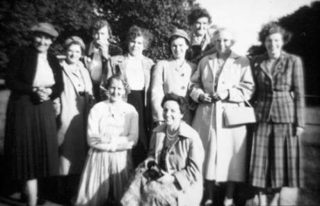 Photograph of ten women posed with trees in the background; they are wearing coats and dresses, and suits; they have been identified as members of Haswell Women's Institute on an outing