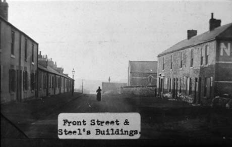Photograph with a typed note reading: Front Street and Steel's Buildings, showing a road running away from the camera; on the right are two-storeyed and one-storeyed terraced houses, and on the right, a block of terraced houses with a chapel-like building behind it; they have been identified as being in Haswell This photograph was submitted by Philip Soakell from the album 'History of Haswell and District', which was compiled by his grandfather Fred Soakell.