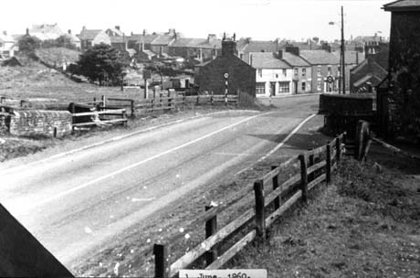 Photograph showing a road running from left to right of the photograph between fences of open fields towards rows of houses; at the approach to the houses a sign imposing a thirty miles an hour limit are on either side of the road; the photograph has been identified as Bank Head Haswell This photograph was submitted by Philip Soakell from the album 'History of Haswell and District', which was compiled by his grandfather Fred Soakell.