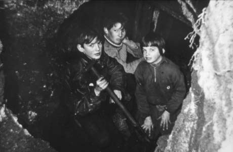 Photograph of three boys, aged between ten and thirteen years, with an indistinct background and a rock face at the right of the picture; one boy is holding the shaft of a tool, possibly a spade; they are wearing jackets and jumpers; they have been identified as digging for coal at Haswell This photograph was submitted by Philip Soakell from the album 'History of Haswell and District', which was compiled by his grandfather Fred Soakell.