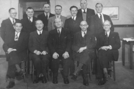 Photograph of twelve men posed in two rows inside a building; they are all wearing suits and ties; thay have been identified as recipients of Haswell I.C.I. Safe Driving Awards