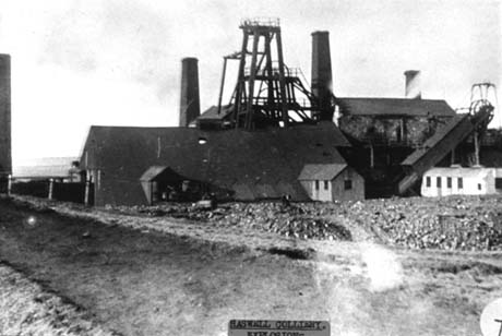 Photograph of the buildings, winding gear, and four chimneys of a colliery, which has been identified as Haswell Colliery This photograph was submitted by Philip Soakell from the album 'History of Haswell and District', which was compiled by his grandfather Fred Soakell.
