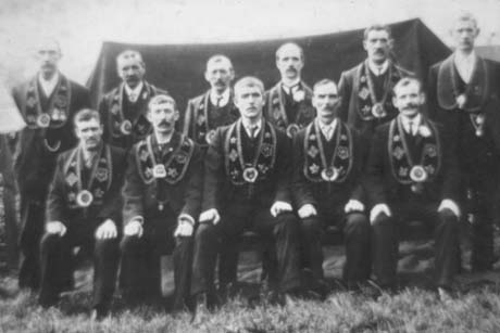 Photograph of eleven men posed in two rows with a tent behind them; they are all wearing the insignia round their necks of the Independent Order of The Good Templars; they have been identified as being connected with Haswell
