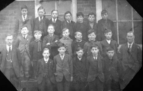 Photograph of nineteen boys, aged approximately thirteen years, posed in three rows outside a brick building; two men, wearing suits and ties, are standing either side of the boys; they have been identified as Mr. Watson and Mr. Stevens and their class in Haswell