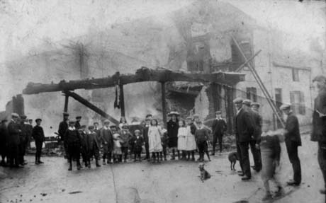 Photograph showing a building the front of which has been damaged by fire; most of the upper floors have been destroyed and only a skeleton remains to indicate where the floor was; a ladder is leaning against the damaged building; a crowd of children and adults is standing in front of the building, most of whom are looking at the camera and away from the building; the fire has been identified as having taken place at Haswell