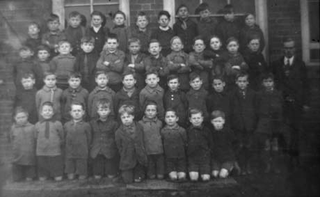 Photograph of forty three boys, aged approximately eight years, posed in four rows in front of a brick building; a man is standing at the right of the group, which has been identified as a school group in Haswell