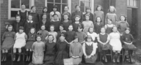 Photograph of thirty five girls, aged approximately six years, posed in four rows in front of a brick building; they have been identified as pupils at a school in Haswell