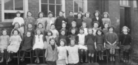 Photograph of thirty four girls aged approximately seven years, posed in four rows outside a brick building; they have been identified as pupils at a school in Haswell