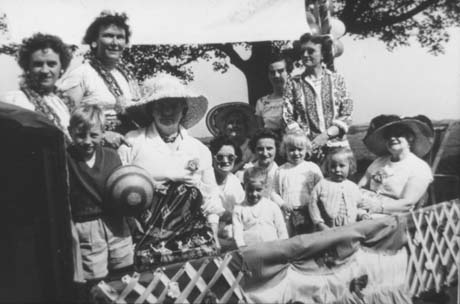 Photograph of eight women, wearing summer clothes and sun hats, standing and sitting behind a decorated border of a float; they are accompanied by four children, aged between approximately three and four years; they have been identified as being on a decorated float and being in Haswell