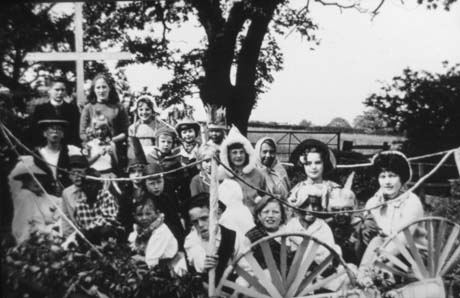 Photograph showing twenty one children, aged between approximately six and fourteen years, in fancy dress on possibly a float; a clergyman and a crucifix can be seen at the left of the picture; they have been identified as members of the Haswell Methodist Church Sunday School