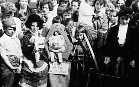 Photograph of a crowd of people, the first row of which, is children in fancy dress; one is dressed as a pirate, one as a Chinaman, another as a Scotsman, and another in a sack with a pig's head sticking out and a notice reading: That's A Pig In A Poke; they have been identified as people attending a Carnival in Haswell