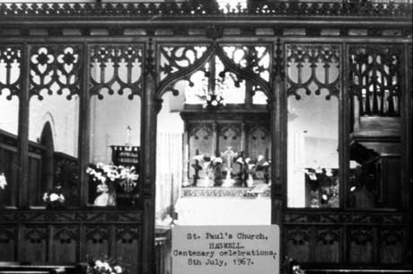 Photograph with a typed note reading: St. Paul's Church, Haswell. Centenary Celebrations, 8th July, 1967, showing the wooden altar screen and the altar beyond; flowers are on the altar and on the left and right of the sanctuary This photograph was submitted by Philip Soakell from the album 'History of Haswell and District', which was compiled by his grandfather Fred Soakell.