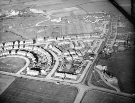 Photograph giving an aerial view of a cross roads with a crescent of semi-detached houses on the left of the cross roads; other semi-detached houses can be seen behind the crescent; a large building can be seen on the right-hand corner of the cross roads; the view has been identified as being in Haswell and what may be the ruins of Haswell Colliery can be seen at the top of the photograph