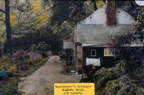 Photograph showing the side of a small house with a flower bed in front and woodland behind; the photograph has a typed note attached which reads: Gamekeeper's Cottages, Elemore Woods, Low Haswell This photograph was submitted by Philip Soakell from the album 'History of Haswell and District', which was compiled by his grandfather Fred Soakell.
