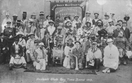 Photograph of forty five people in fancy dress, posed in four rows, holding musical instruments; behind them is a banner with the words Regd. Under War Charities Act Haswell Social Club Charitable ---ct B--d; in front of them are the words, Haswell Club Rag Time Band 1919