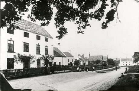 Photograph showing, on the left-hand side, the exterior of a large house with, beyond it, two four smaller houses; beyond the houses the side of the exterior of the church can be seen and the front of another house can be seen; on the right-hand side of the photograph grassed areas can be seen; eleven indistinct figures of children can be seen; the photograph has been identified as Hawthorn Village