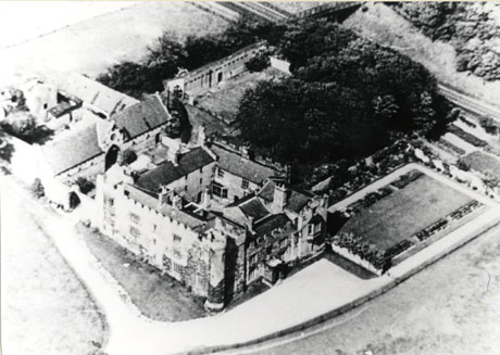 Photograph of an aerial view of a castellated building constructed round a courtyard, showing ancillary buildings, gardens and woodland; the photograph has been identified as Aerial View, Hawthorn Towers, 1950's